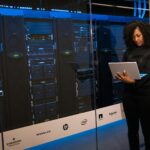 Une ingénieure utilisant un ordinateur portable tout en surveillant des serveurs de données dans une salle de serveurs moderne.