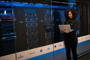 Une ingénieure utilisant un ordinateur portable tout en surveillant des serveurs de données dans une salle de serveurs moderne.