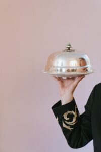 Gros plan d'un serveur tenant un plateau de service en argent sur un fond rose clair.
