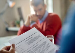 Un candidat tient son CV face à un recruteur. L'image est floue à l'arrière-plan, mettant l'accent sur le document, pour illustrer la création CV.