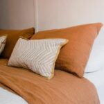 Chambre minimaliste avec coussins beiges et terracotta apportant une ambiance chaleureuse et apaisante.