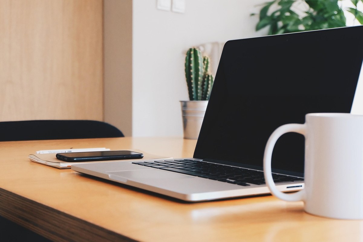 Espace de travail avec ordinateur portable, téléphone, carnet et tasse sur bureau en bois