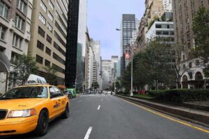 Rue de Manhattan avec taxi jaune stationné, immeubles de hauteur variée et arbres en arrière-plan