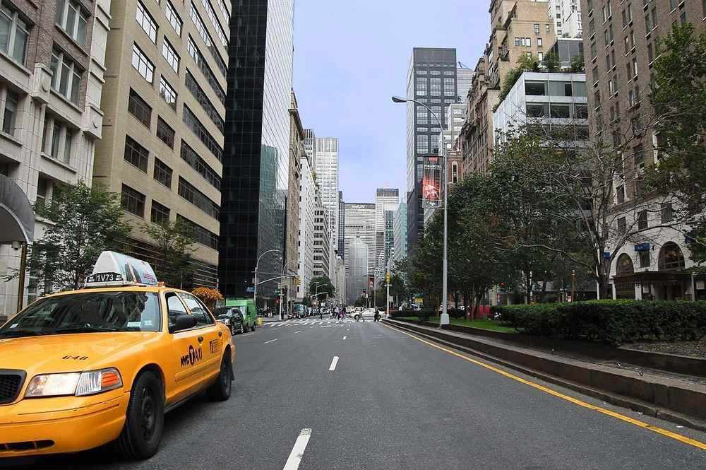 Rue de Manhattan avec taxi jaune stationné, immeubles de hauteur variée et arbres en arrière-plan