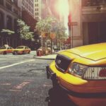 Taxi jaune à l'avant, deux taxis derrière, rue urbaine ensoleillée