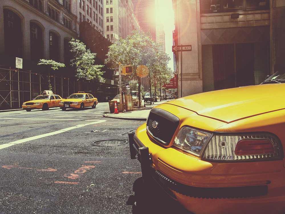 Taxi jaune à l'avant, deux taxis derrière, rue urbaine ensoleillée
