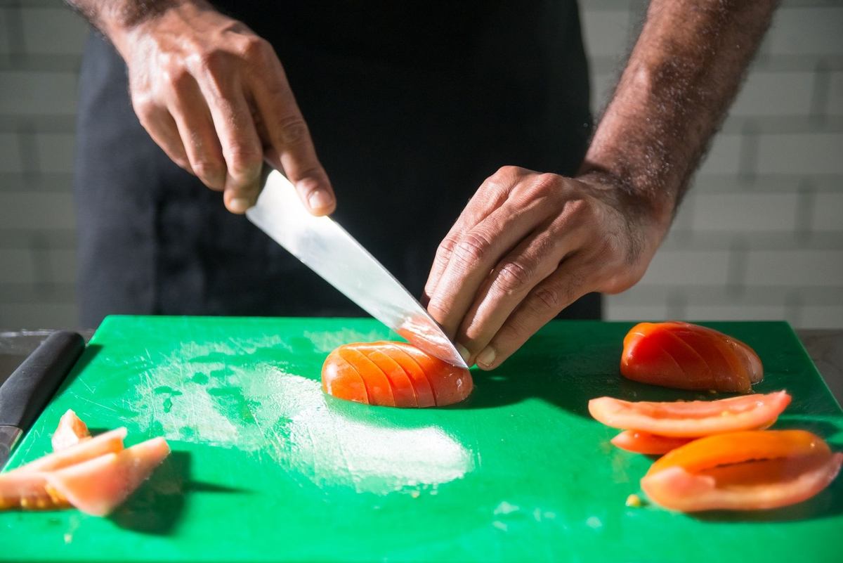 Une personne coupe des tomates sur une planche verte avec un couteau Une personne coupe des tomates sur une planche verte avec un couteau