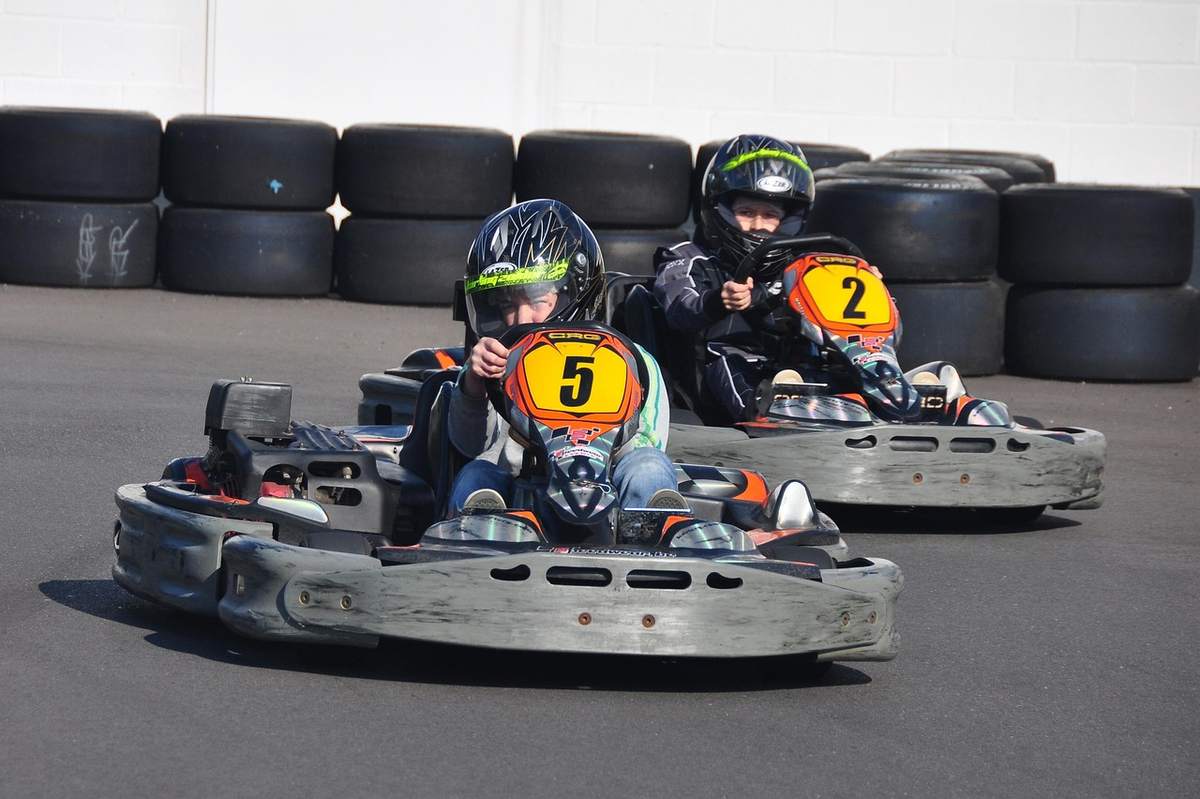Deux personnes en karting sur une piste avec des pneus de voitures en arrière-plan