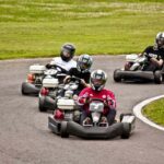 Quatre personnes en karting sur une piste avec un gazon à l'arrière-plan